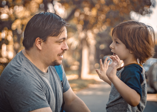 Father sitting across from son outside and smiling