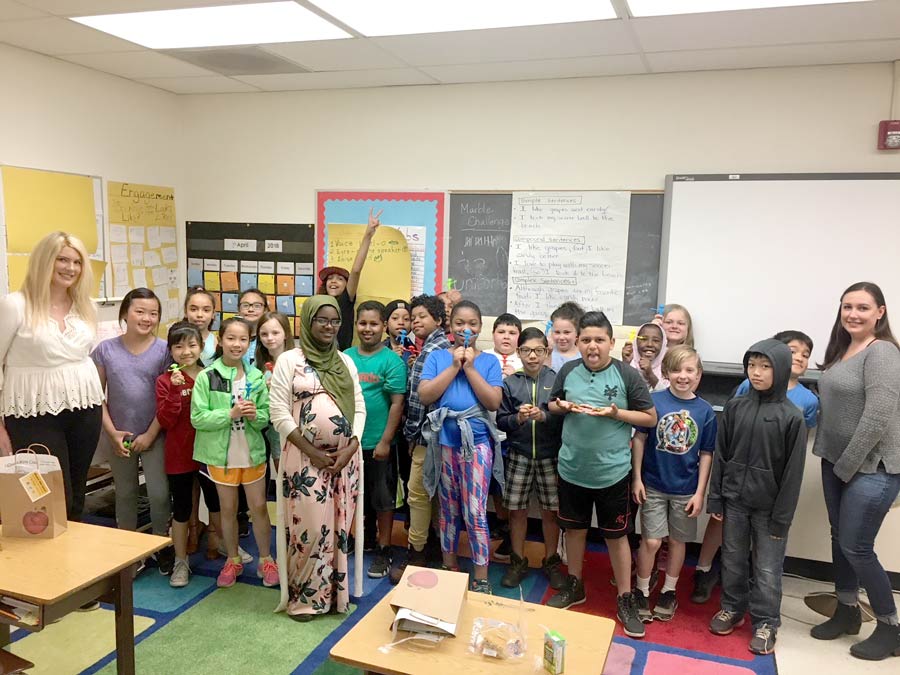 large group of fourth grade students in a classroom smiling for the camera with a unitus branch employee on either end