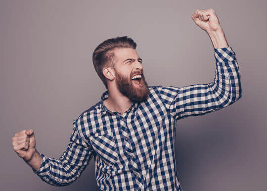 Unitus Go Savings: Young, bearded man in checkered shirt pumping fists in air with excitement.