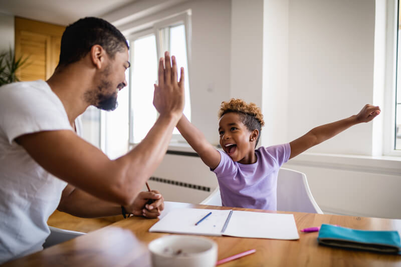 father and daughter high five as he helps her with her homework