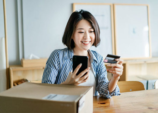 Alegre mujer de negocios comprando en Internet con su smartphone y pagando con tarjeta de crédito.