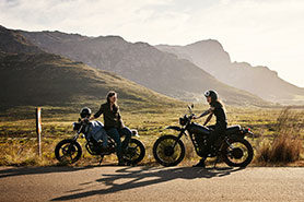 Two young women riding their motorcycles through the countryside.