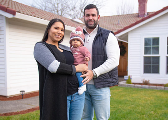 feliz pareja hispana delante de su nueva casa