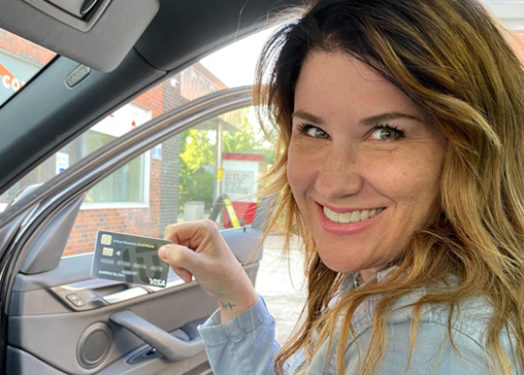 woman in car holding up a credit card