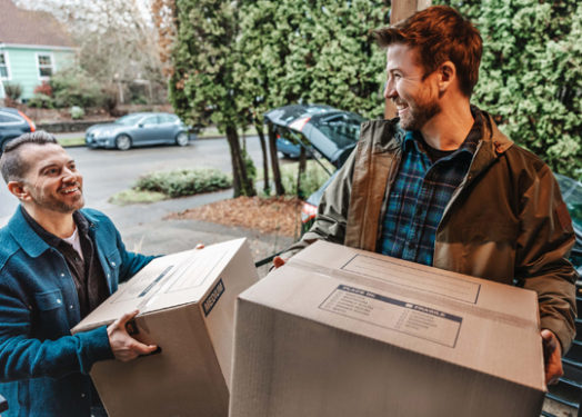 two men carrying moving boxes into house